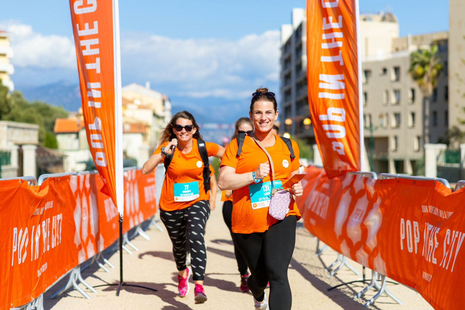 Femmes en orange qui courent et qui sourient en passant la ligne d'arrivée d'une course entre filles organisée à Lyon