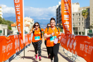 Femmes en orange qui courent et qui sourient en passant la ligne d'arrivée d'une course entre filles organisée à Lyon