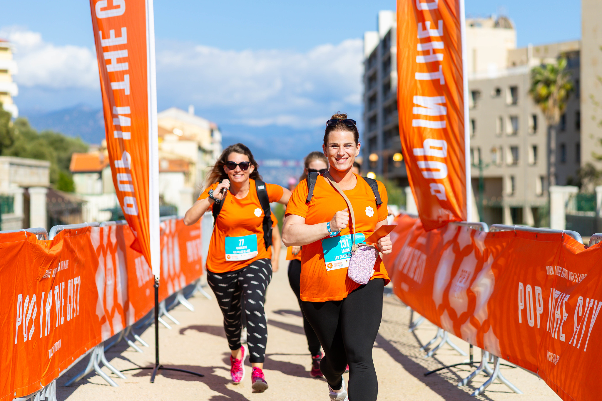 Femmes en orange qui courent et qui sourient en passant la ligne d'arrivée d'une course entre filles organisée à Lyon